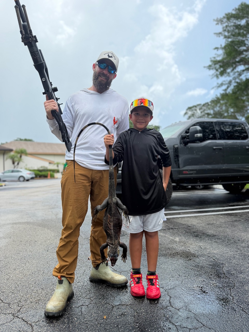 Adult and child holding a harvested iguana beside an air rifle after a South Florida hunt