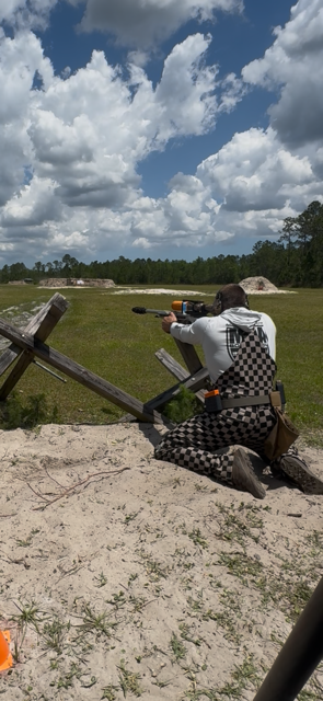 Precision rifle competitor engaging a target from a kneeling barricade position