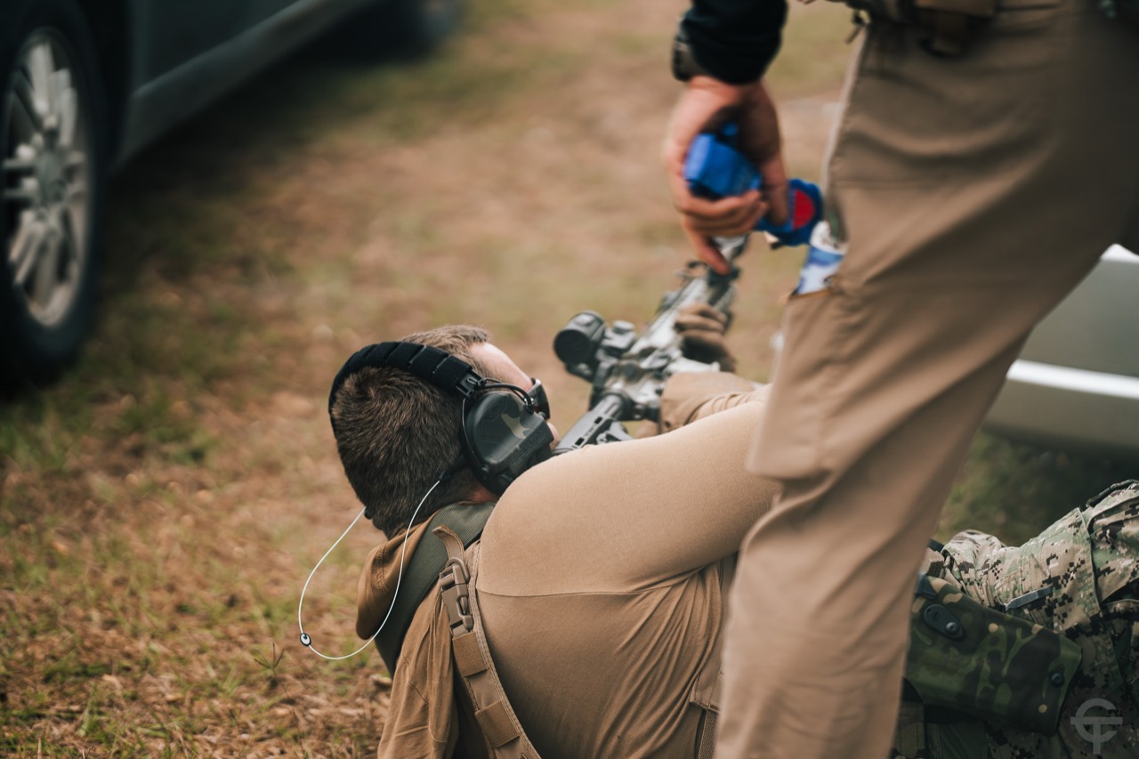 Instructor providing hands-on guidance to a prone rifle shooter during a supervised exercise