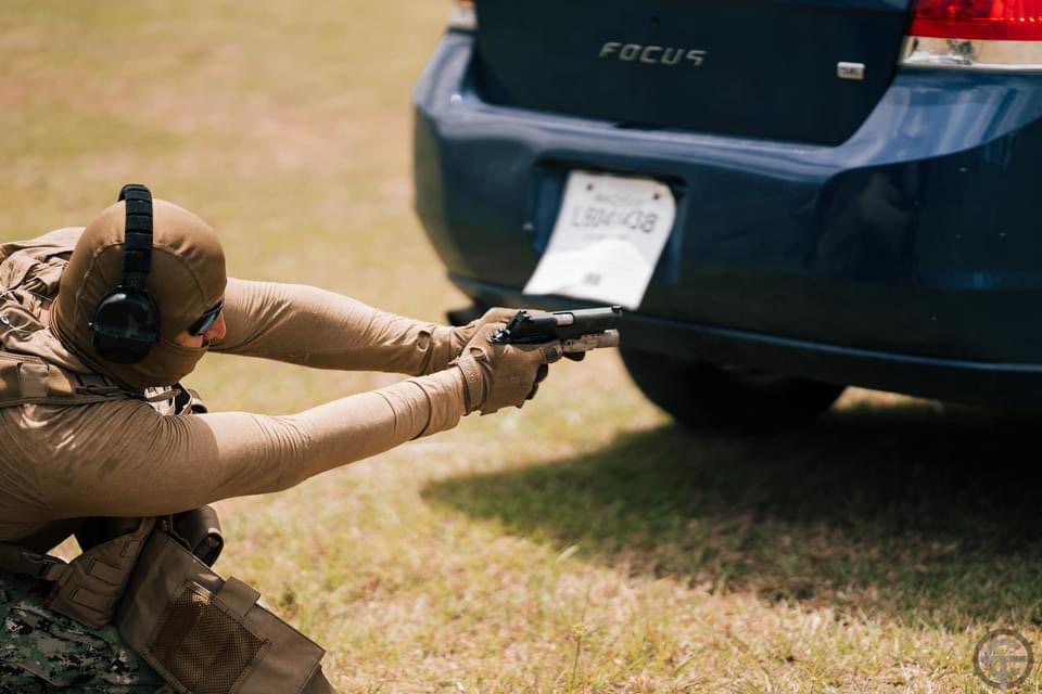 Shooter practicing a controlled pistol position beside the rear of a vehicle